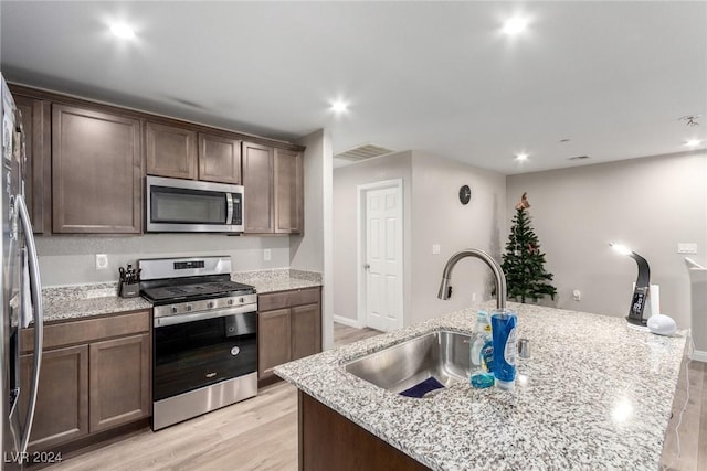 kitchen with stainless steel appliances, visible vents, a sink, an island with sink, and light stone countertops