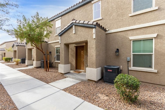 entrance to property featuring central AC, a tile roof, and stucco siding