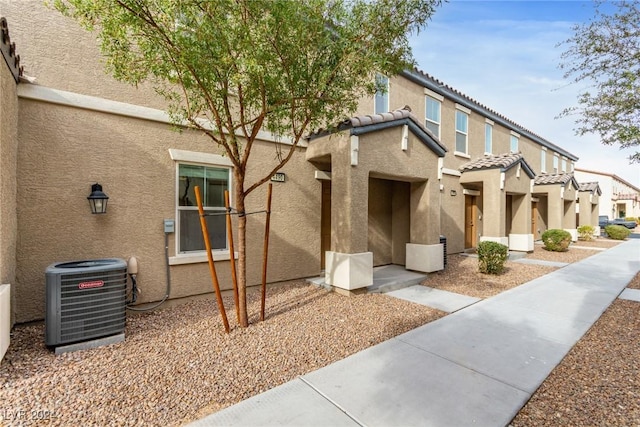 exterior space featuring a tiled roof, cooling unit, and stucco siding