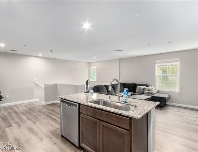 kitchen with a sink, light wood-style floors, stainless steel dishwasher, and open floor plan