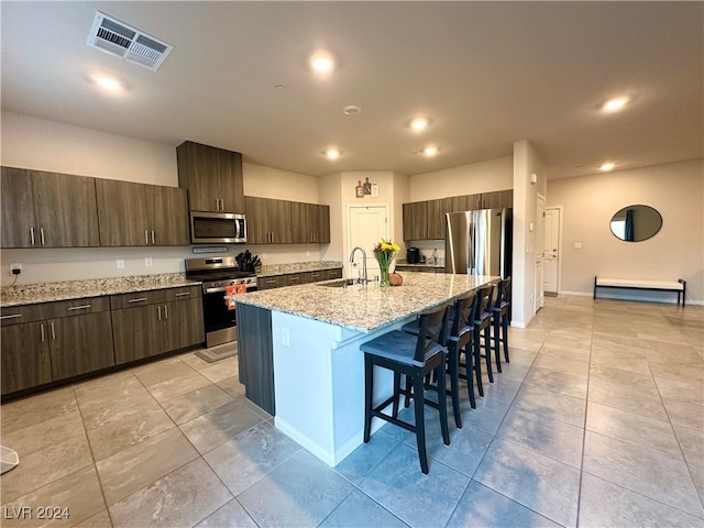 kitchen featuring a breakfast bar, stainless steel appliances, visible vents, a sink, and dark brown cabinetry