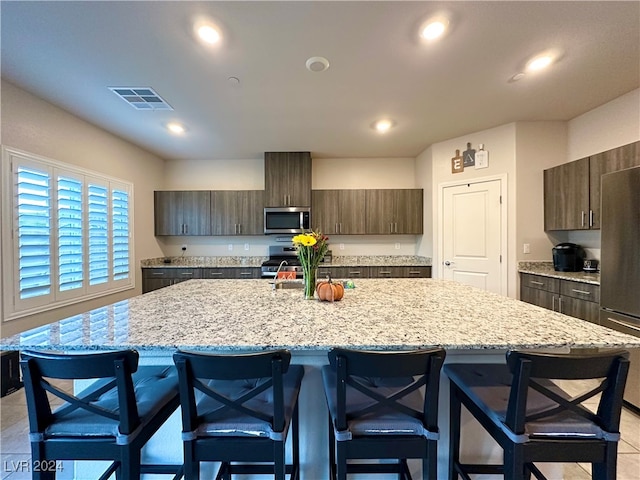 kitchen with a kitchen island with sink, recessed lighting, stainless steel appliances, a breakfast bar, and visible vents