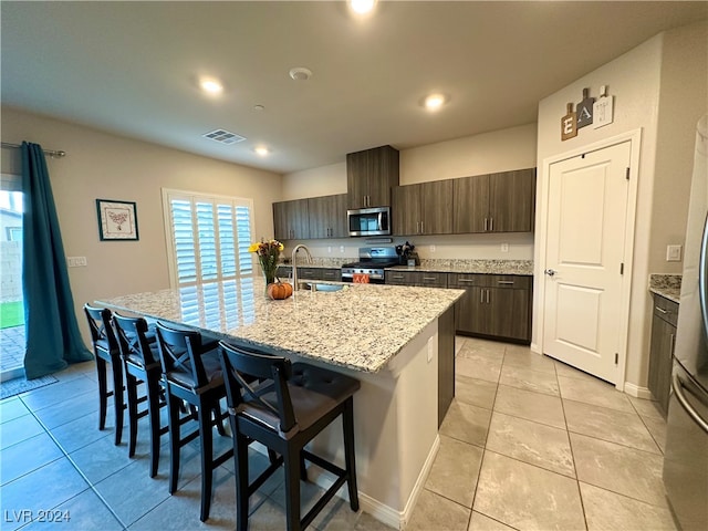 kitchen featuring a center island with sink, a breakfast bar area, stainless steel appliances, visible vents, and a sink