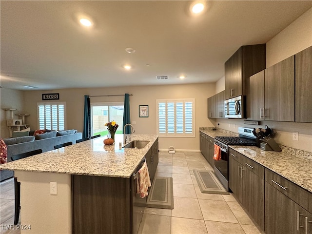 kitchen with light tile patterned flooring, stainless steel appliances, a sink, visible vents, and a center island with sink