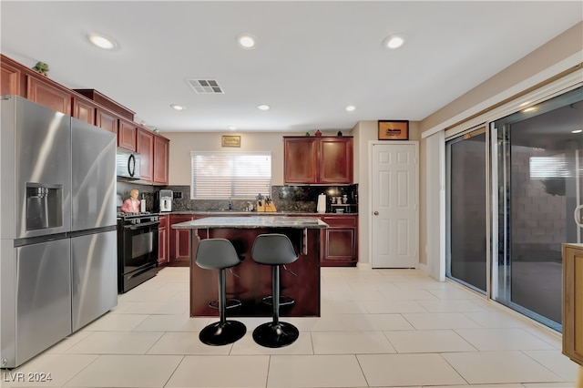 kitchen featuring a center island, decorative backsplash, light tile patterned floors, a kitchen bar, and stainless steel appliances