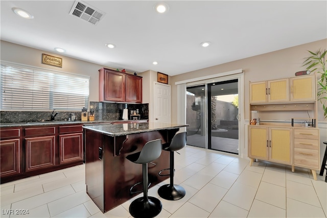 kitchen with sink, tasteful backsplash, a kitchen breakfast bar, dark stone countertops, and a kitchen island