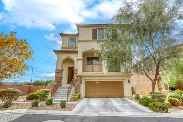 mediterranean / spanish home featuring a balcony, driveway, an attached garage, stucco siding, and stone siding