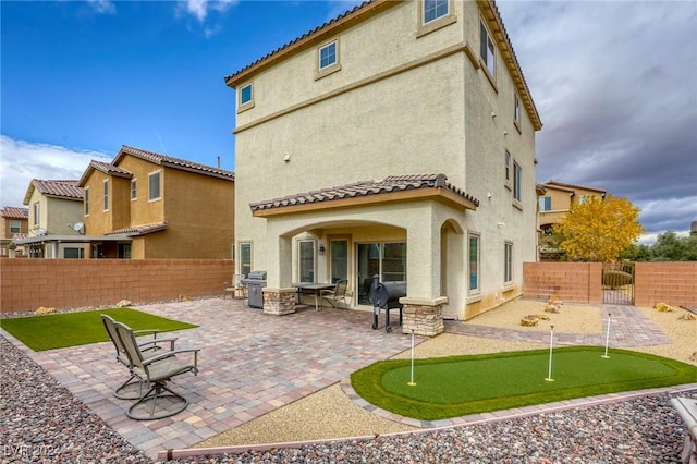 rear view of house featuring stucco siding, a gate, a tile roof, fence private yard, and a patio area