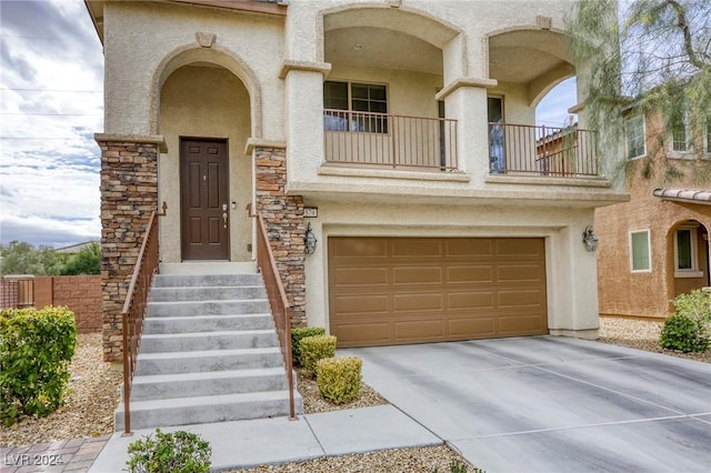 view of front of property with stucco siding, driveway, stone siding, a garage, and a balcony