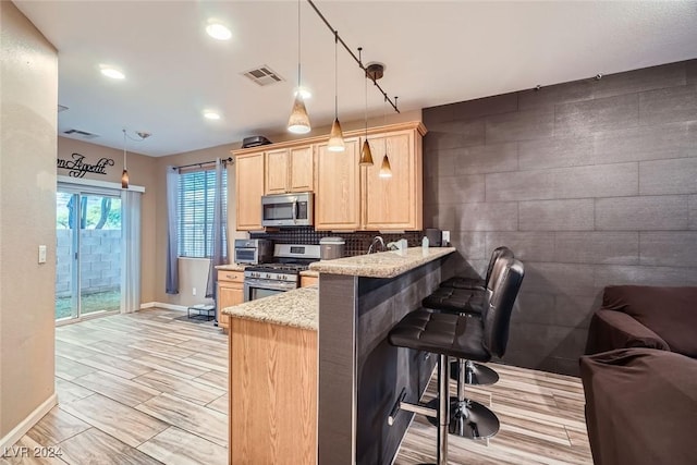 kitchen featuring light brown cabinetry, appliances with stainless steel finishes, hanging light fixtures, kitchen peninsula, and a breakfast bar