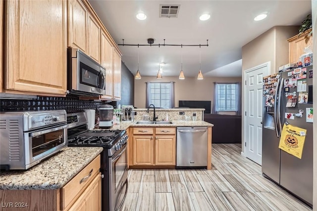 kitchen featuring sink, track lighting, kitchen peninsula, pendant lighting, and stainless steel appliances