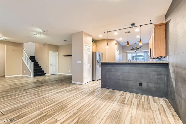 kitchen with hanging light fixtures, track lighting, sink, kitchen peninsula, and stainless steel fridge