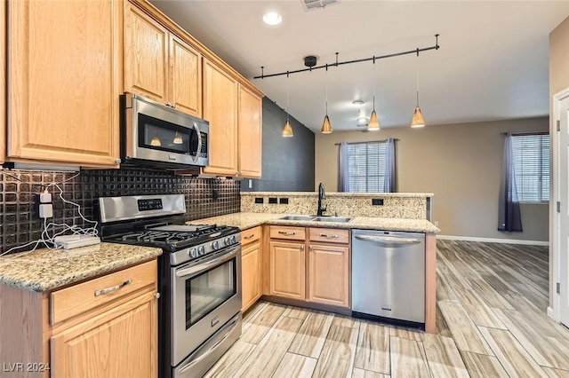 kitchen with sink, kitchen peninsula, pendant lighting, stainless steel appliances, and light stone counters