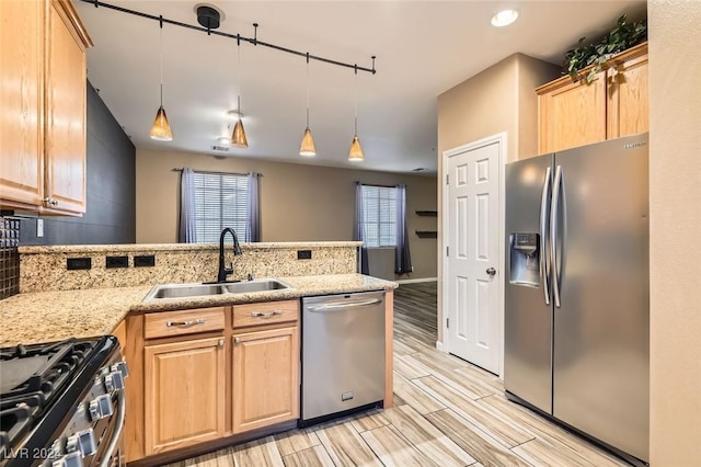 kitchen featuring kitchen peninsula, light brown cabinetry, sink, decorative light fixtures, and stainless steel appliances