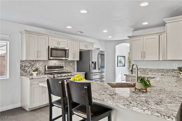 kitchen with light stone countertops, sink, stainless steel appliances, a kitchen breakfast bar, and kitchen peninsula