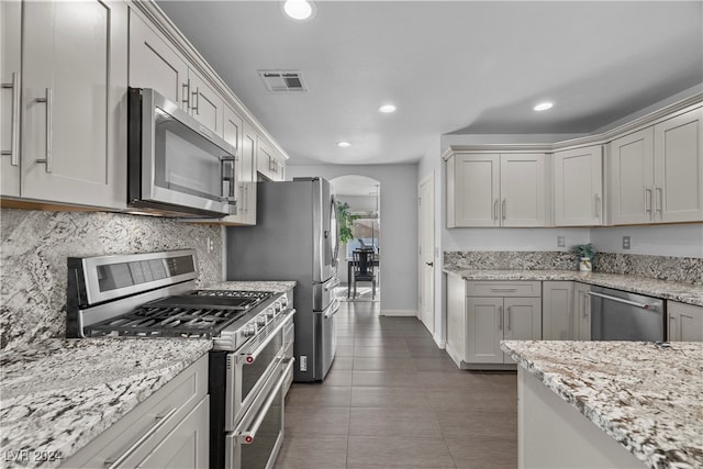 kitchen with decorative backsplash, appliances with stainless steel finishes, dark tile patterned floors, and light stone countertops