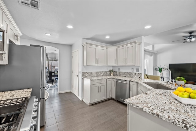 kitchen featuring kitchen peninsula, appliances with stainless steel finishes, light stone counters, sink, and white cabinets