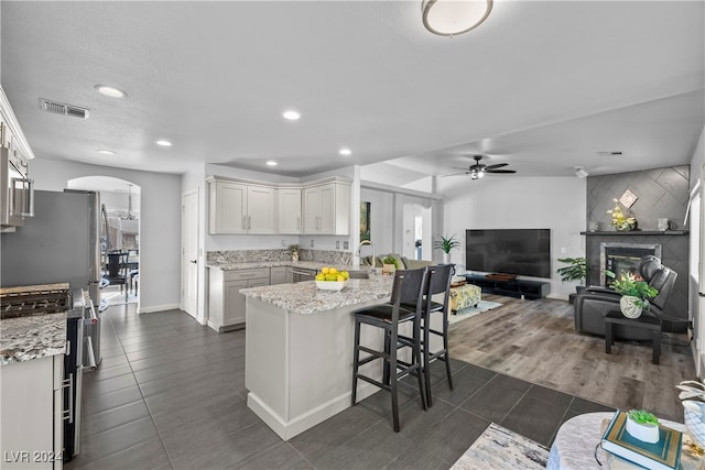 kitchen with dark wood-type flooring, light stone countertops, white cabinetry, a kitchen bar, and kitchen peninsula