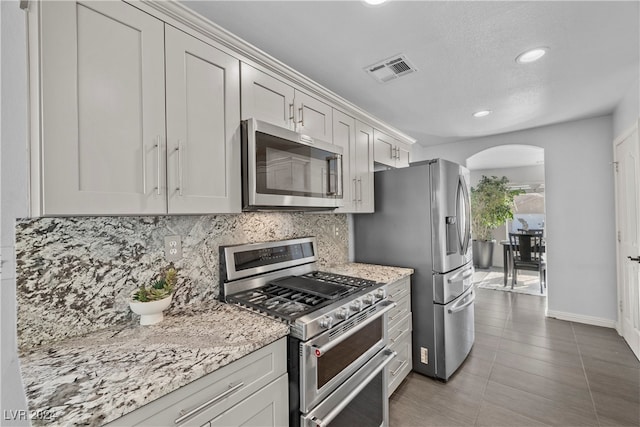 kitchen featuring dark tile patterned floors, light stone countertops, stainless steel appliances, and tasteful backsplash