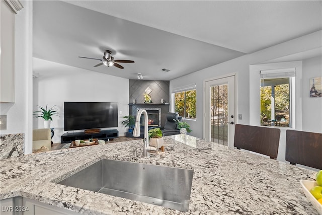 kitchen with a wealth of natural light, sink, ceiling fan, and light stone countertops