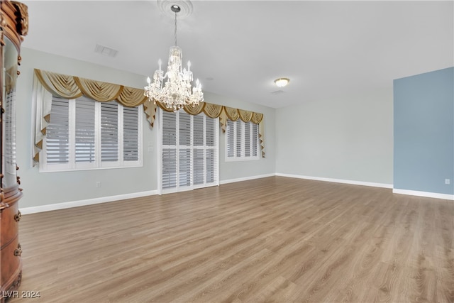 unfurnished room featuring a notable chandelier and light hardwood / wood-style flooring