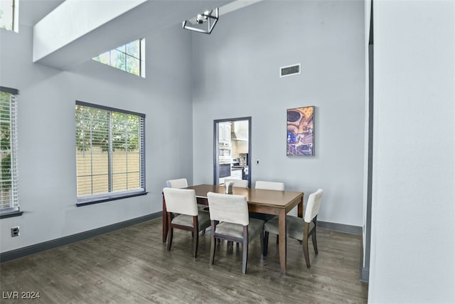 dining space with a towering ceiling, dark hardwood / wood-style floors, and a notable chandelier