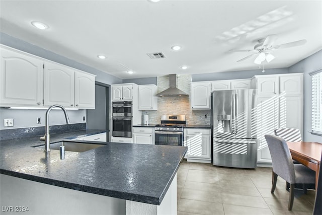 kitchen with kitchen peninsula, appliances with stainless steel finishes, sink, wall chimney range hood, and white cabinets