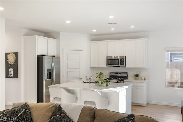 kitchen featuring appliances with stainless steel finishes, sink, a center island with sink, light hardwood / wood-style flooring, and white cabinets