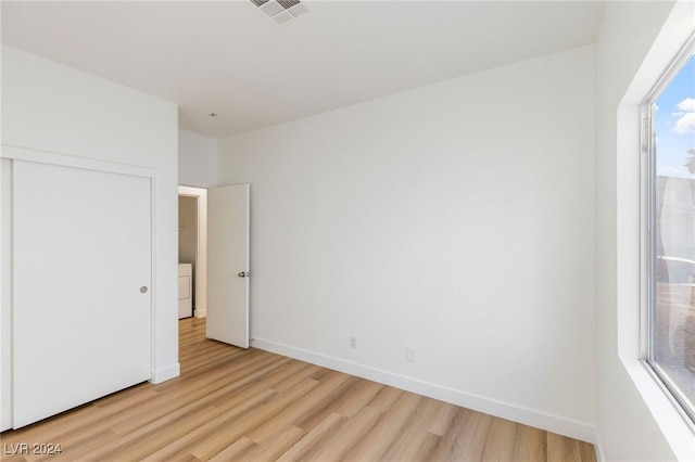 unfurnished bedroom featuring washer / clothes dryer, visible vents, baseboards, a closet, and light wood finished floors