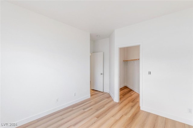 unfurnished bedroom featuring light wood-type flooring, a spacious closet, baseboards, and a closet