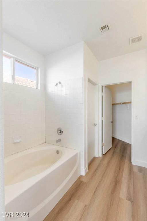 full bathroom with washtub / shower combination, visible vents, baseboards, and wood finished floors