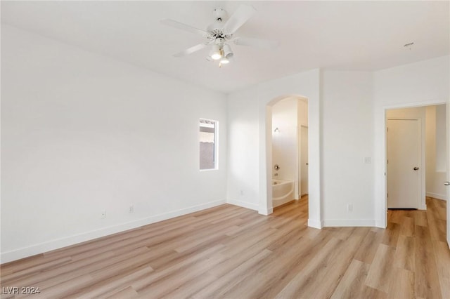 spare room featuring light wood-style floors, arched walkways, ceiling fan, and baseboards