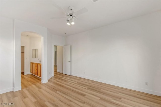 unfurnished room with arched walkways, light wood finished floors, a ceiling fan, and baseboards