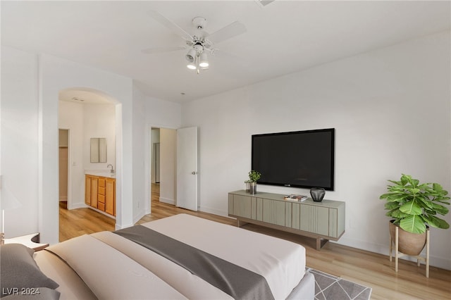 bedroom with arched walkways, light wood finished floors, a ceiling fan, ensuite bath, and baseboards