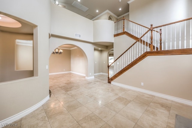 interior space featuring a towering ceiling, an inviting chandelier, crown molding, and light tile patterned flooring