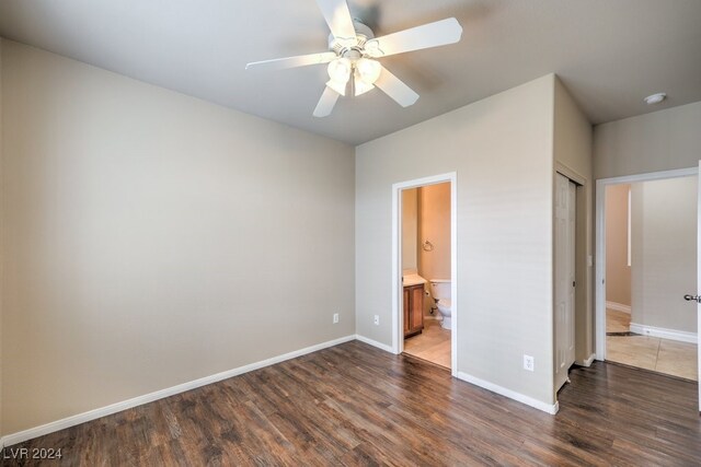 unfurnished bedroom with ceiling fan, a closet, dark wood-type flooring, and ensuite bath