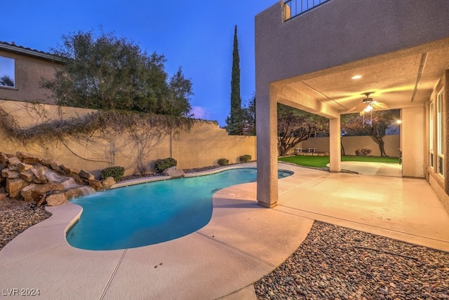 pool at dusk with a patio area, ceiling fan, and pool water feature