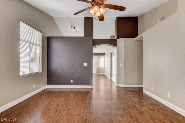 unfurnished living room featuring arched walkways, wood finished floors, visible vents, and baseboards