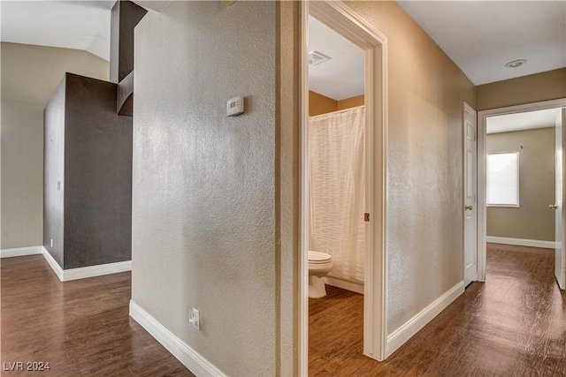 hallway featuring visible vents, baseboards, dark wood-type flooring, and a textured wall