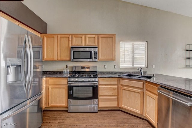 kitchen featuring stainless steel appliances, dark countertops, lofted ceiling, light brown cabinets, and a sink