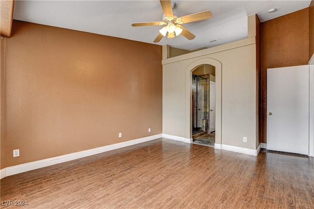 spare room featuring arched walkways, ceiling fan, wood finished floors, and baseboards