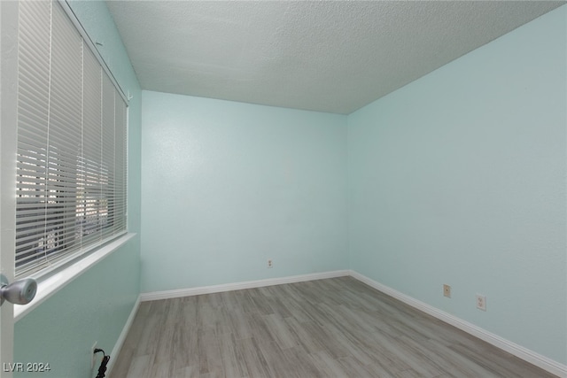 empty room with a textured ceiling and light hardwood / wood-style flooring