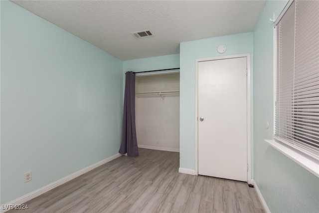 unfurnished bedroom with light wood-type flooring, a textured ceiling, and a closet