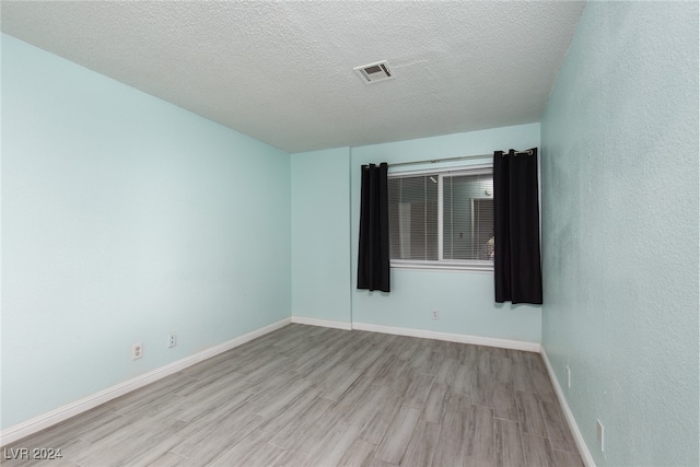 empty room with a textured ceiling and light hardwood / wood-style floors