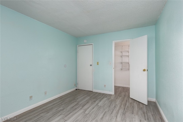 unfurnished bedroom with light hardwood / wood-style floors, a walk in closet, a textured ceiling, and a closet