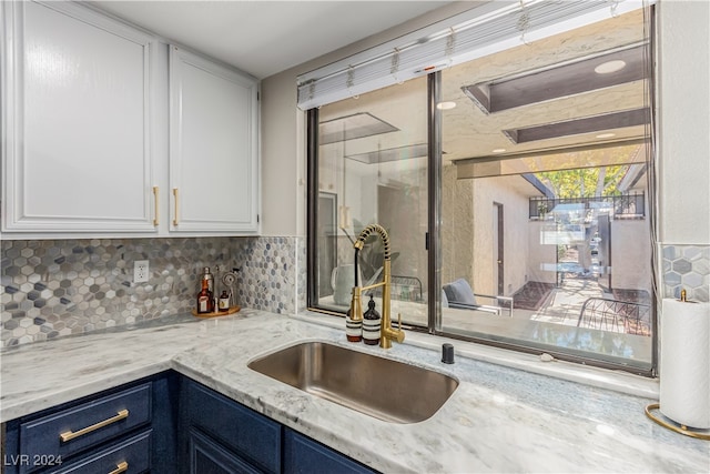 kitchen with blue cabinets, tasteful backsplash, sink, white cabinets, and light stone countertops