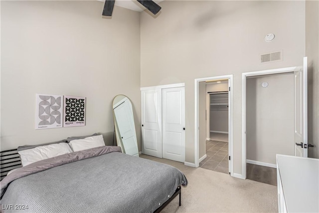 carpeted bedroom with beamed ceiling, ceiling fan, a closet, and a high ceiling