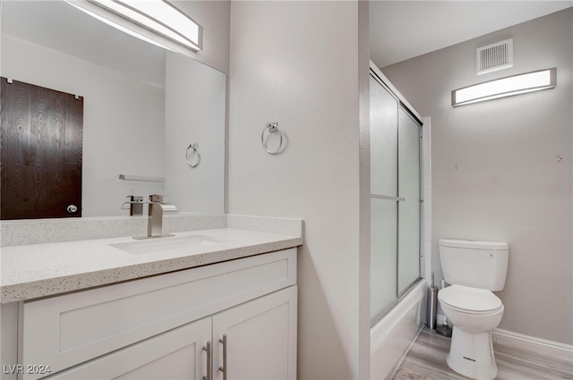 full bathroom featuring toilet, vanity, combined bath / shower with glass door, and hardwood / wood-style flooring