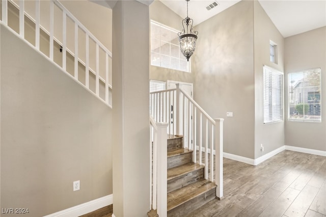 staircase featuring a towering ceiling, an inviting chandelier, and hardwood / wood-style flooring