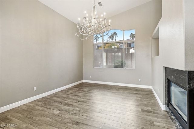 unfurnished dining area featuring hardwood / wood-style flooring, a high end fireplace, high vaulted ceiling, and an inviting chandelier